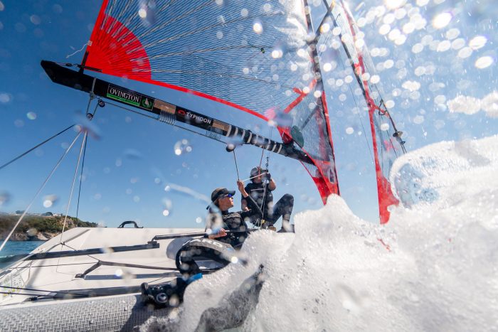 Water splashes as two sailors direct their boat.