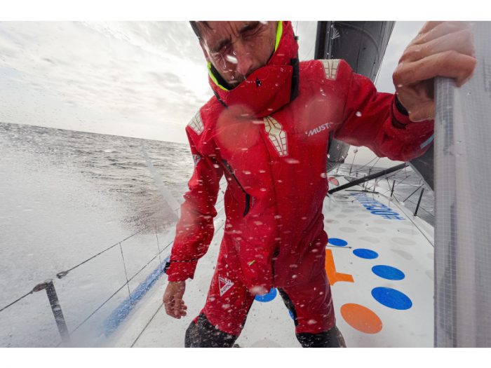 A sailor braving the elements on his boat while wearing a Musto sailing jacket.