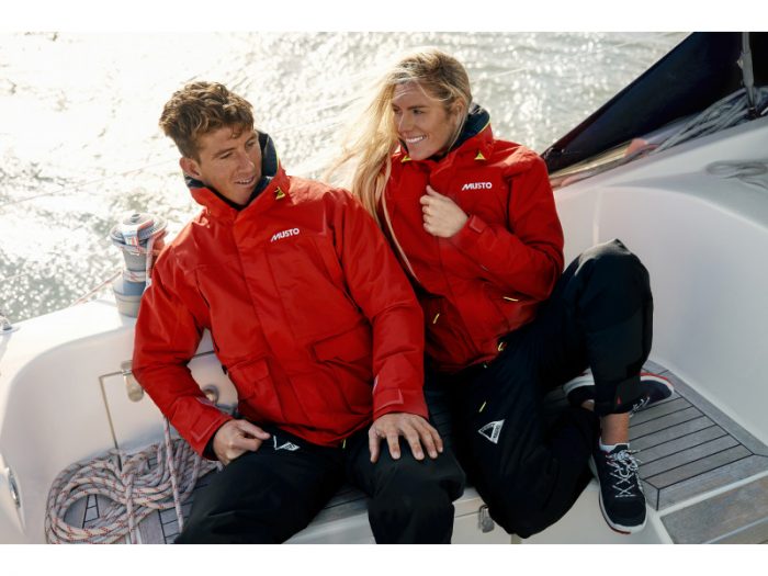 A man and woman wearing Musto sailing jackets while sat on a boat.